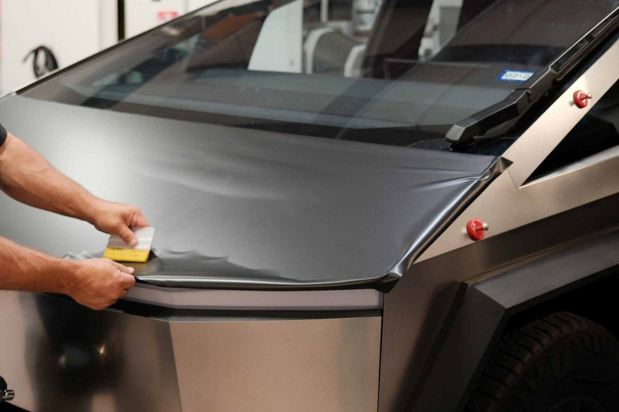 A man carefully applies a sticker to the hood of a car, enhancing its appearance with a vehicle wrap design.